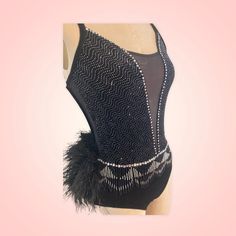 a woman's black leotard with feathers and beads on the bottom, in front of a pink background