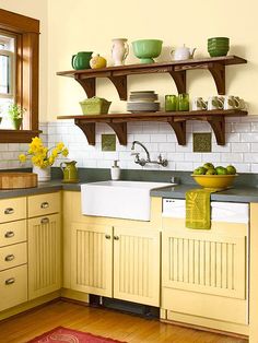 a kitchen with yellow cabinets and green dishes on the shelf above the sink is decorated with flowers