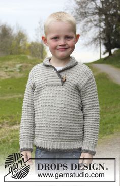 a young boy standing in the middle of a road wearing a sweater with buttons on it