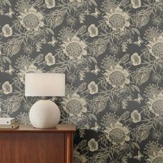 a white vase sitting on top of a wooden table next to a wallpaper covered in flowers