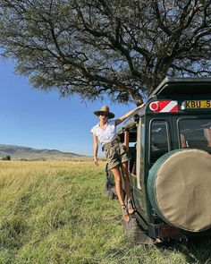 a woman standing on the back of a green truck next to a tree and grass field