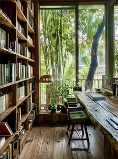 a wooden table sitting under a window next to a book shelf filled with lots of books