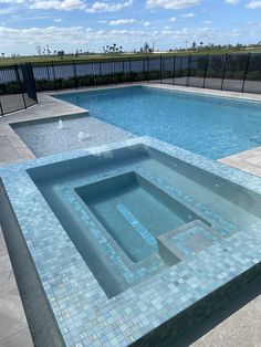 an empty swimming pool with tiled sides and blue tiles on the bottom, in front of a fenced area