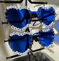 two blue sunglasses with white letters on them sitting on top of a metal stand next to each other