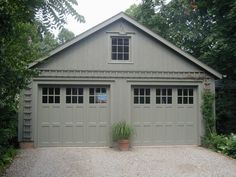 a garage with two doors and a plant in the front yard, surrounded by greenery