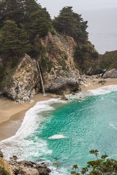 an ocean beach with waves crashing on the shore and trees in the background, along with a waterfall