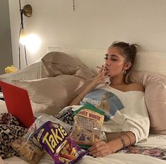 a woman laying in bed with her laptop and snacks