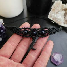 a hand holding a black string bracelet with beads and a crescent pendant on it's end