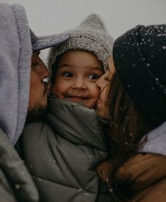 a man and woman kissing while holding a small child in their arms, with snow on the ground behind them