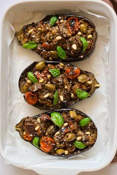 three stuffed eggplant halves in a white dish with basil leaves and sunflower seeds