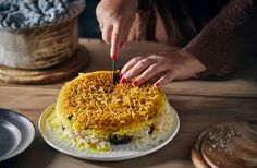 a woman cutting into a cake on top of a wooden table next to other plates