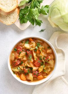 a white bowl filled with pasta soup next to bread and parsley on a table