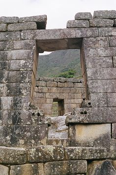 an open window in the side of a stone structure with mountains in the background,