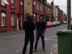 two men standing in the middle of a street talking to each other and one is holding a trash can