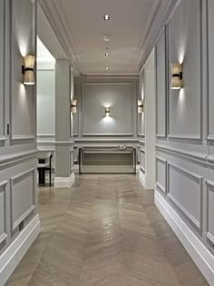 a long hallway with white walls and wood floors is lit by two wall sconces