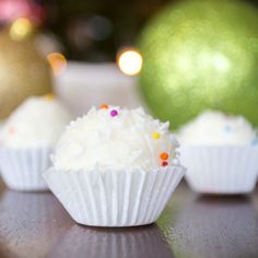 three cupcakes with white frosting and sprinkles sitting on a table