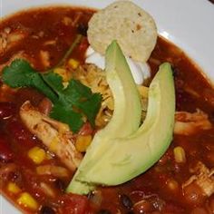 a white bowl filled with chicken tortilla soup and topped with avocado