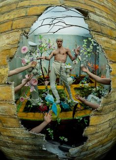 a man standing on top of a wooden table surrounded by plants and flowers in front of a mirror