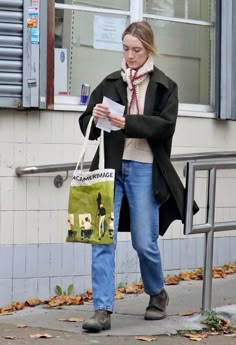 a woman is walking down the street with her shopping bag in hand and looking at something