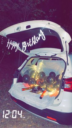 the back end of a white car with balloons and lights in it's trunk