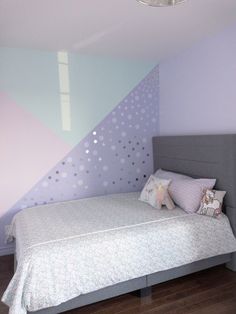 a bed sitting in a bedroom next to a wall painted purple and blue with polka dots