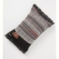 a black and grey pillow with fringes on it's sides, sitting on a white surface