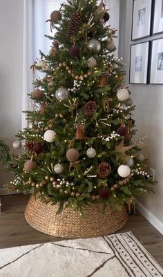 a small christmas tree with ornaments in a basket on the floor next to a window