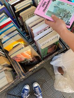 a person holding a book in front of a pile of books on the ground with their feet up