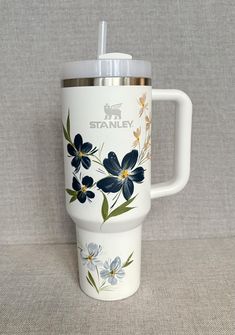 a white travel mug with blue flowers painted on the side and a stainless steel lid