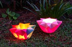 two paper lamps sitting on the ground next to some grass and plants in the background