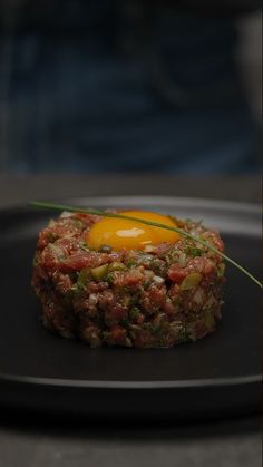 a black plate topped with an egg on top of meat