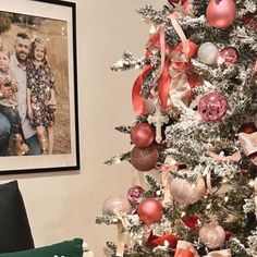 a christmas tree is decorated with red, pink and silver ornaments while a family photo hangs on the wall