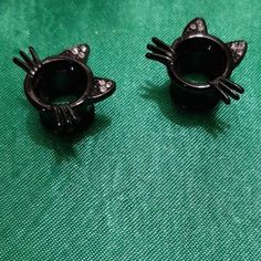 two black cat shaped rings sitting on top of a green cloth