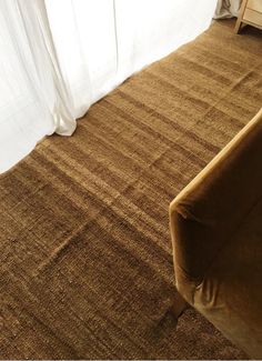 a brown couch sitting on top of a wooden floor next to a white curtained window