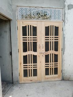 two wooden doors with intricate designs on them in front of a concrete wall and cement floor