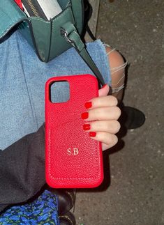 a woman holding a red cell phone case in her hand and purse on the ground