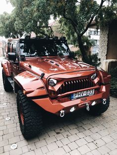 a red jeep parked in front of a tree on a brick sidewalk next to a building