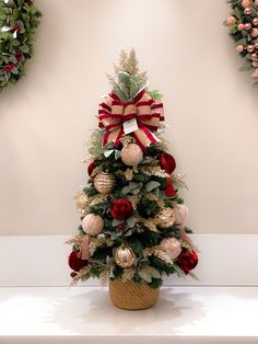 a small christmas tree with red and gold ornaments on it's top, in front of two wreaths