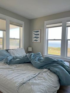 an unmade bed sitting in front of two windows with blue sheets on it and white pillows