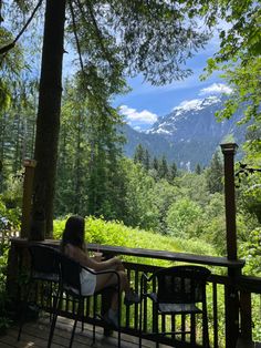 a woman sitting on top of a wooden deck next to a forest filled with trees