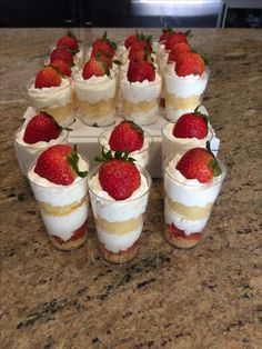 strawberries are arranged on top of small desserts in plastic cups sitting on a marble countertop