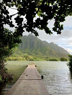 two people are standing on the end of a dock in front of some water and mountains