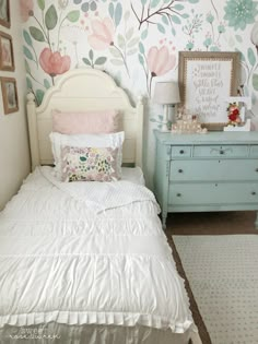 a white bed sitting in a bedroom next to a wall with flowers on it's side