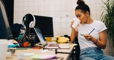 a woman sitting in front of a computer holding a cup