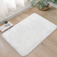 a white area rug on the floor next to a potted plant and two books