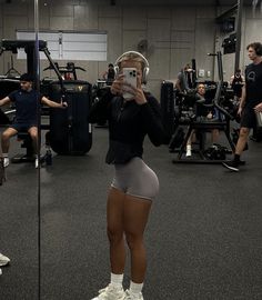 a woman in grey shorts and headphones standing next to a mirror with other people behind her