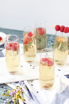 three glasses filled with champagne and raspberries on a table