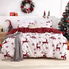 a bed covered in red and white sheets with reindeer print on it, next to a christmas tree