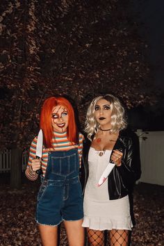 two women dressed in costumes standing next to each other holding knives and knifes, with trees behind them