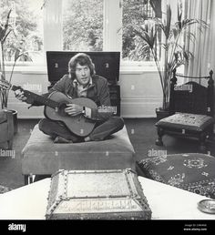 an old black and white photo of a man playing guitar in his living room - stock image